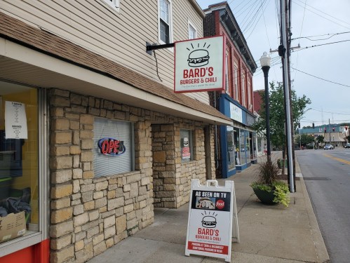 Sign for Bard's Burgers & Chili outside a restaurant, with an "Open" sign and a promotional board on the sidewalk.