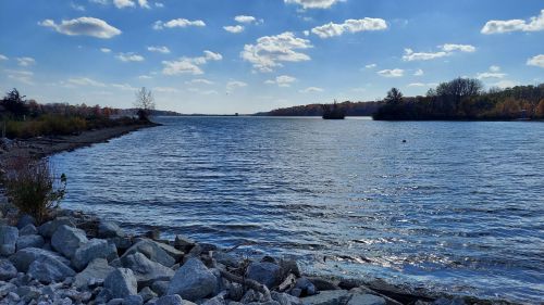 A serene river scene with rocky shorelines, blue water, and a clear sky dotted with clouds.