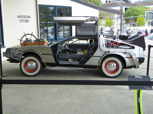 A DeLorean car with gullwing doors, displayed outside a museum store, featuring futuristic modifications and details.