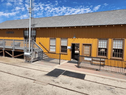 A yellow wooden building with multiple windows and a ramp, set against a blue sky with scattered clouds.