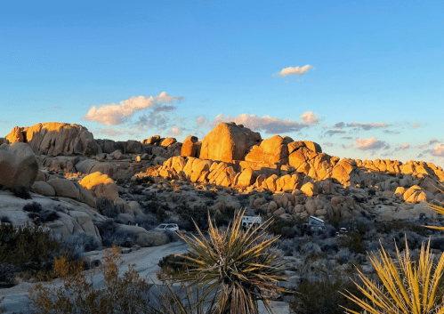 Sunset over rocky desert landscape with scattered clouds and desert vegetation in the foreground.