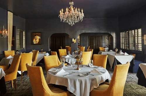 Elegant restaurant interior with round tables, yellow chairs, and a chandelier, creating a sophisticated dining atmosphere.