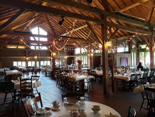 A spacious rustic restaurant interior with wooden beams, tables set for dining, and warm string lights.