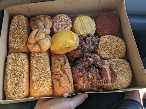 A box filled with various donuts, including glazed, sprinkled, and frosted varieties, arranged neatly.
