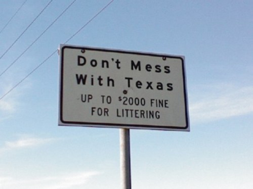 Sign reading "Don't Mess With Texas" with a warning about a $2000 fine for littering. Clear blue sky in the background.