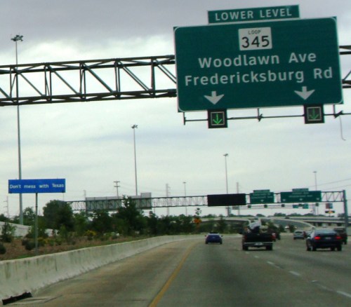 Highway sign indicating Woodlawn Ave and Fredericksburg Rd, with a "Don't mess with Texas" sign in the background.
