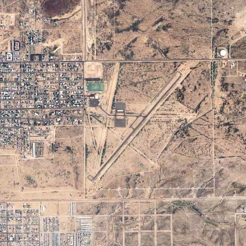 Aerial view of a small town surrounded by desert, featuring roads, buildings, and a sports field.