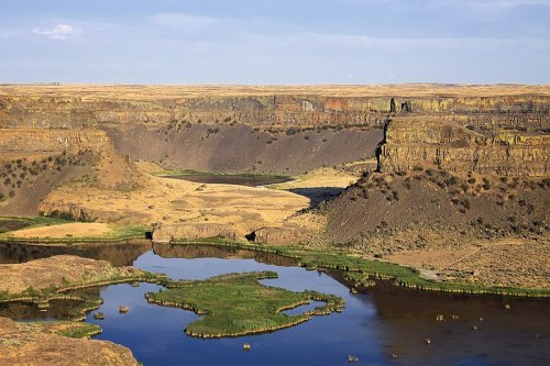 A scenic view of a canyon with a river, surrounded by rocky cliffs and grassy areas under a clear blue sky.