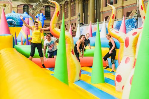 A colorful inflatable obstacle course with people jumping and playing in a lively indoor setting.