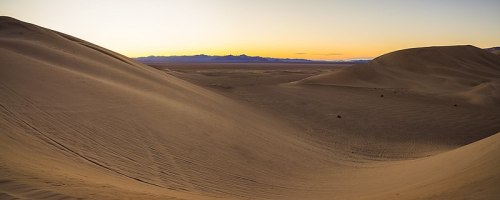 A serene desert landscape at sunset, featuring rolling sand dunes and a colorful sky in the background.