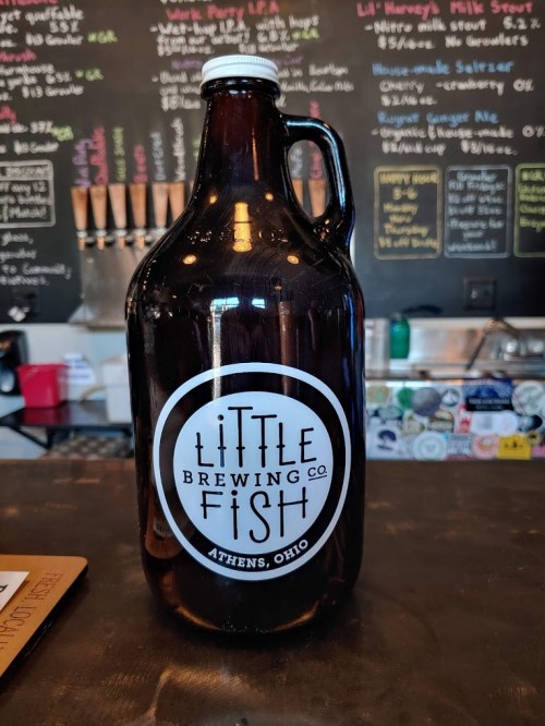 A brown glass growler from Little Fish Brewing Co. in Athens, Ohio, displayed on a wooden surface.
