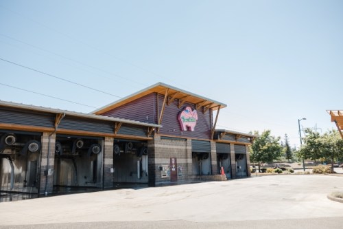 A modern building with a pink pig logo, featuring wooden accents and a clear blue sky in the background.