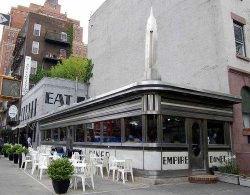 A classic diner with a silver exterior and outdoor seating, located on a city street.