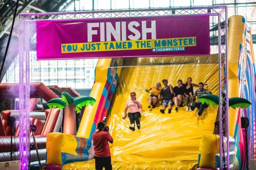 A group of people sliding down a large inflatable slide with a "FINISH" banner above, celebrating their fun experience.