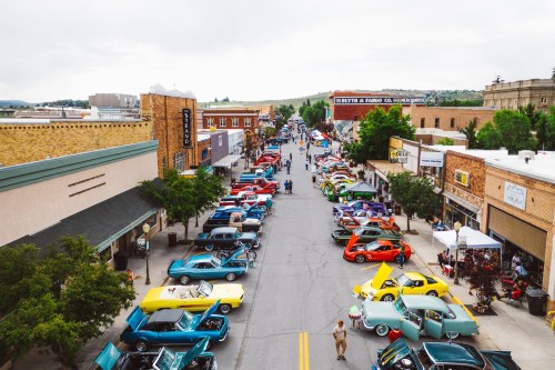 Aerial view of a vibrant street filled with classic cars and people enjoying a car show on a cloudy day.