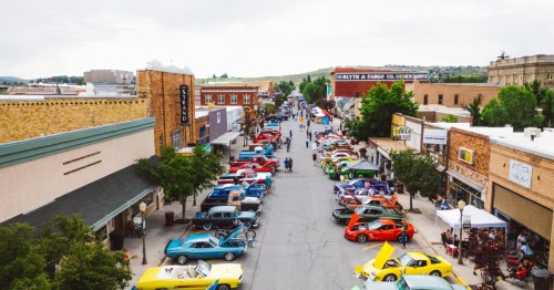 A vibrant street lined with classic cars and people, showcasing a lively car show in a small town.