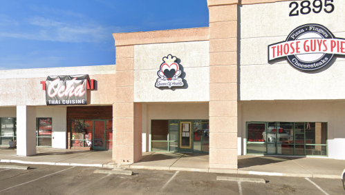 Exterior view of a shopping plaza featuring Thai cuisine and cheesesteak restaurants, with clear blue skies above.
