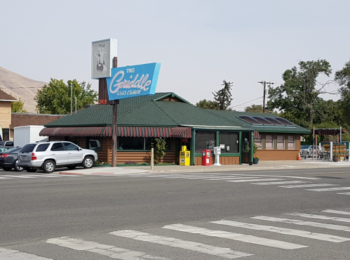 A roadside restaurant with a green roof and sign reading "The Griddle," surrounded by trees and parked cars.