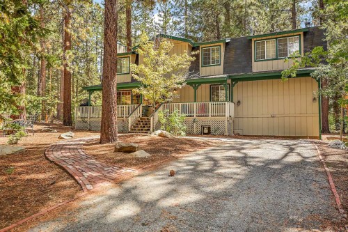 A two-story house surrounded by tall trees, with a stone pathway leading to the entrance and a front porch.
