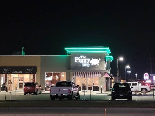A nighttime view of The Piggy BBQ restaurant, featuring neon lights and a welcoming entrance.