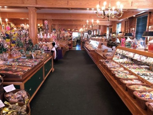 A colorful candy shop interior with shelves filled with various sweets and treats, warmly lit by chandeliers.