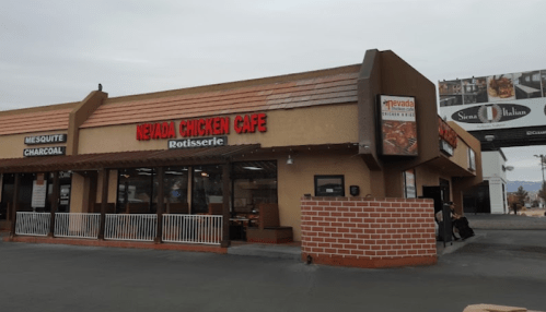 Exterior of Nevada Chicken Cafe, featuring a rotisserie sign and a brick wall, with a cloudy sky in the background.
