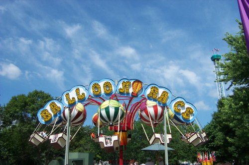 Colorful amusement park ride with hot air balloon designs under a blue sky with fluffy clouds.