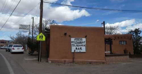 A rustic adobe building with a sign for "Perera's Restaurant & Tijuana Bar" on a roadside under a blue sky.