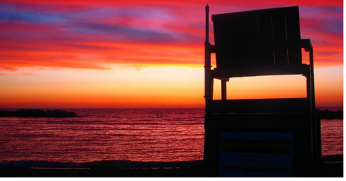 Silhouette of a lifeguard chair against a vibrant sunset over the ocean.
