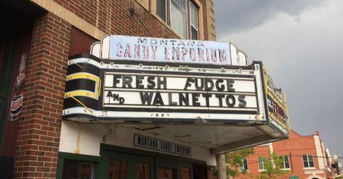 Sign for Montana Candy Emporium featuring "Fresh Fudge" and "Walnettos" against a cloudy sky backdrop.