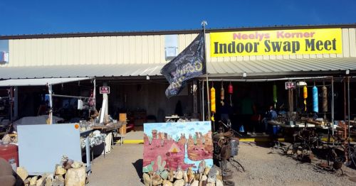 A colorful sign reads "Neely's Korner Indoor Swap Meet" outside a market with various items for sale.