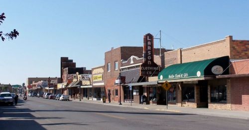 A small town street lined with shops, featuring a vintage sign for Larson Clothing Co. and a green awning.
