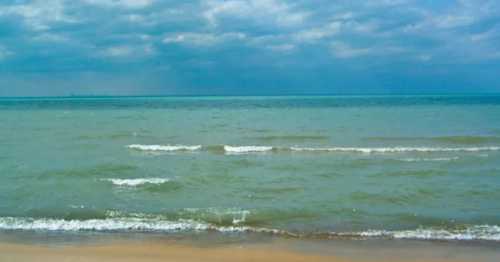 A calm beach scene with gentle waves lapping at the shore under a cloudy sky.