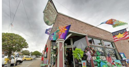 A colorful storefront with various flags and decorations, set against a cloudy sky. A yellow car is parked nearby.
