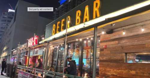 A lively beer bar with bright signage and outdoor seating, illuminated at night in an urban setting.