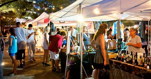 A lively outdoor market scene with vendors, colorful tents, and people browsing various handmade goods and crafts.