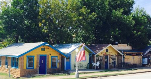 Colorful small houses with a large tree and an American flag in front, creating a charming street scene.