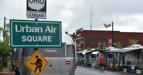 Sign for Urban Air Square in Logan, Ohio, with Airstream trailers and a guitar-playing warning sign in view.