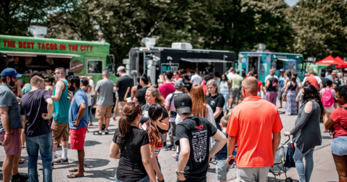 A busy outdoor food festival with people gathered around various food trucks on a sunny day.