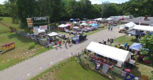 Aerial view of a bustling outdoor market with tents, vendors, and people walking along a pathway.