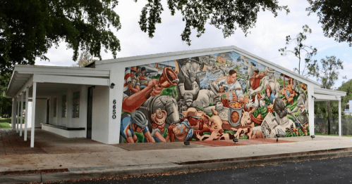 A colorful mural depicting various scenes of community life and culture on the side of a building.