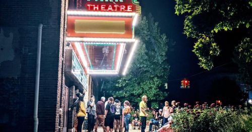 A crowd gathers outside a brightly lit theater at night, with a marquee sign reading "Theatre."