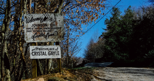Signpost welcoming visitors to Johnson County, home of Loretta Lynn and birthplace of Crystal Gayle, along a gravel road.