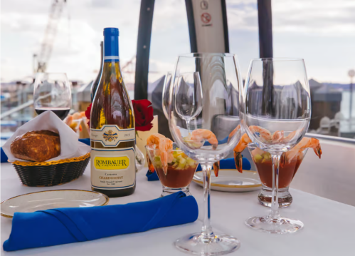 A dining table set with wine, shrimp cocktails, and glasses, overlooking a scenic waterfront view.