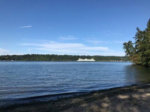 A serene lake view with clear blue skies, surrounded by lush green trees and distant hills.