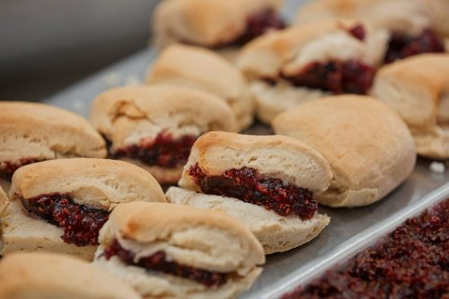 Freshly baked biscuits filled with a rich, red fruit jam, arranged on a baking tray.