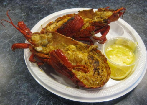 Two cooked lobsters on a white plate, served with a small cup of melted butter and a lemon wedge.
