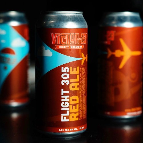A close-up of a can of Flight 305 Red Ale from Victor 23 Craft Brewery, featuring a colorful design with an airplane motif.