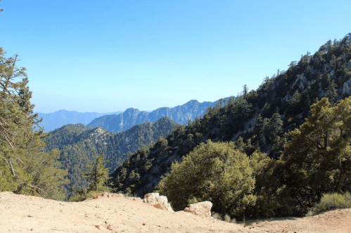 A scenic view of mountains and trees under a clear blue sky, showcasing a rugged landscape.