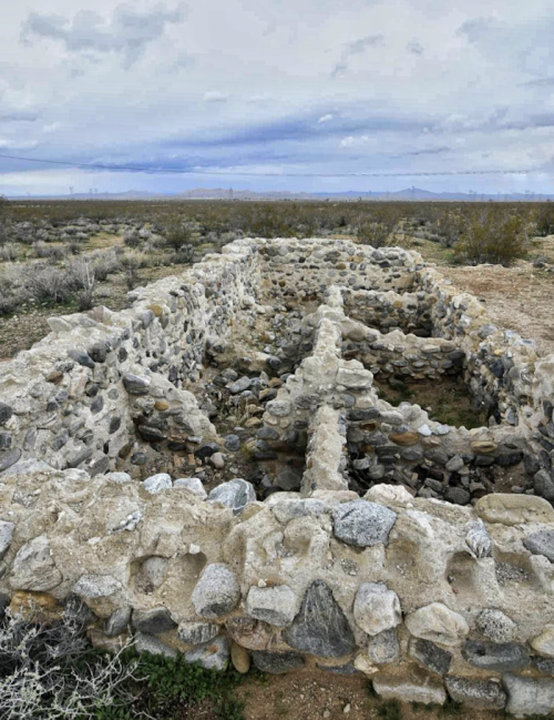 Ruins of a stone structure in a barren landscape, with cloudy skies and sparse vegetation surrounding it.